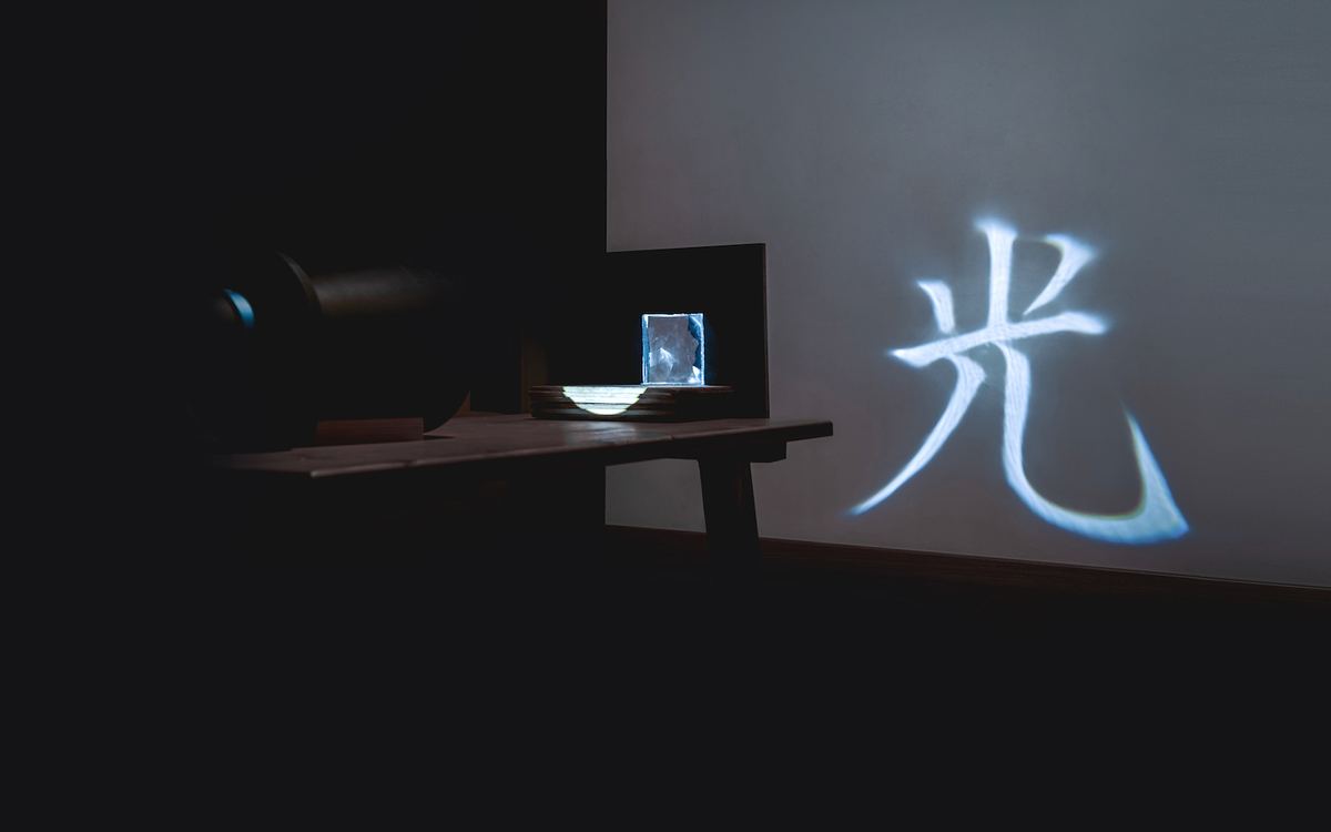 A lens projecting the character 光 (“light” in Chinese and Japanese) onto a screen.